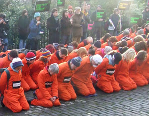 People in orange boiler suits emulation the submission position imposed on prisoners held in the US base in Guantanamo.