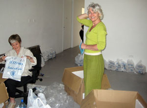 Jane Frere in olive green cottons smiling as a seated volunteer puts figures in a Scotmid bag