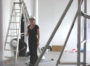 Woman in a white hard hat, standing between a step ladder and the foot of a scaffolding rig