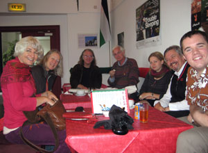 Smiling people sit round the red covered table in Wassim's Lebanese cafe , El-Daar