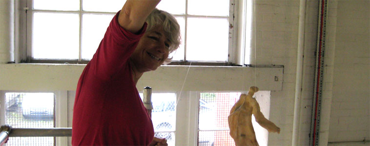 Close up of Jane on the scaffold platform, smiling as she holds a 31cm figure on its wire and looks at it