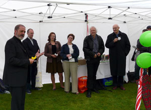 Ewan Aitken holding a yellow paper lotus flower speaks as people watch on