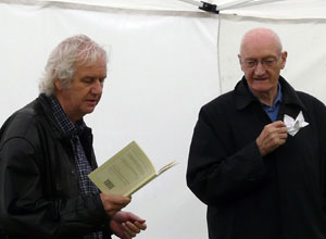 Makar Ron Butlin reads poetry from a book as Richard Holloway stands listening