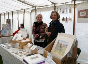 Two smiling women behind a table covered in prints