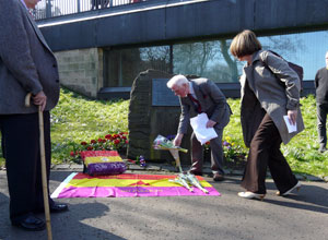 Elderly man and a woman stooping to place bouquets by the stone