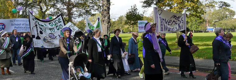 People in Edwardian costume marching along Melville Drive with banners