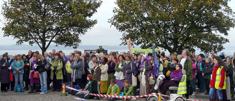 A crowd on Calton Hill listens to Cathy Peattie singing  with the Firth of Forth and Fife in the background 