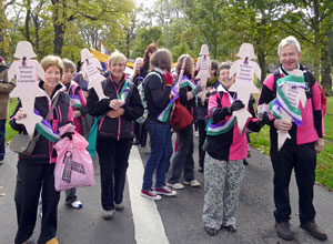 Women and men in black and pink waterproofs holding up  cutout pink figures