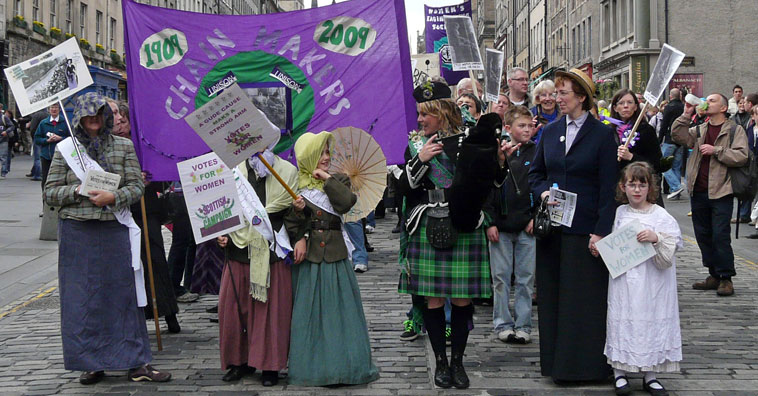 People in Edwardian costume marching along Melville Drive with banners
