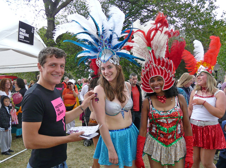 An Amnesty International acitvist puts a  "Protect the Human" sticker on the arm of a  dancer from Edinburgh Samba School, as they relax after the parade