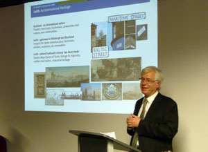 Mark talking with a projection of Leith street scenes behind him.