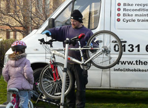 Man fixes bicycle suspended on a stand while a girl looks on