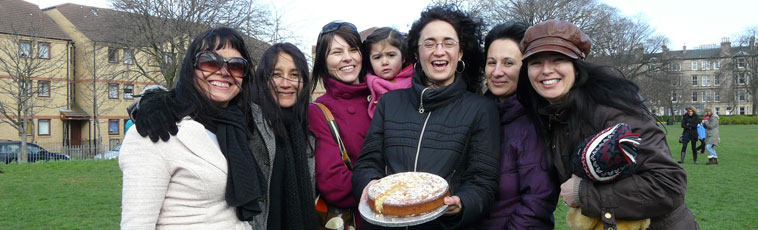 Six smiling women with a child holding up the winning almond cake in Montgomery St Park