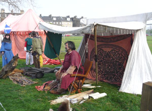 Bearded man in crimson with a full figure, sits surrounded by skins, furs and  arrows