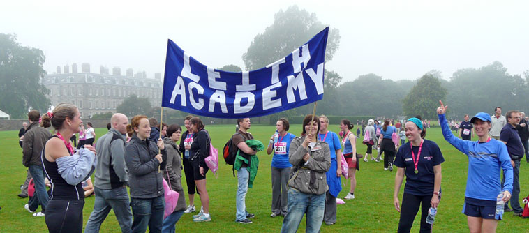 Leith Academy banner (white letters on blue) with Holyrood Palace behind in the mist. and various staff and pupils