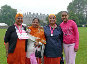 Four women in orange and pink smiling with Holyrood Palace in the background