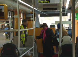 Man in yellow safety jacket on the deck at the front of the tram talking to two mature women