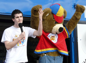 Man in white tee shirt with a bear in a red, yellow and blue cap dressed as an old fashioned school boy