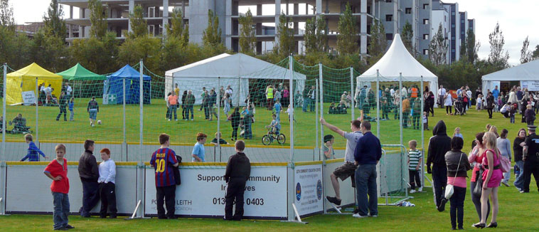 Netted and boarded area surrounded by young people with flats under construction in the background