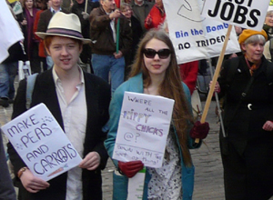 Young man and woman with posters "MAKE PEAS AND CARROTS" and "WHERE ARE ALL THE HIPPY CHICKS @?