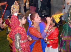 A woman in red crouches to add the finishing touches to a little bou's make up, as a little girl watches on
