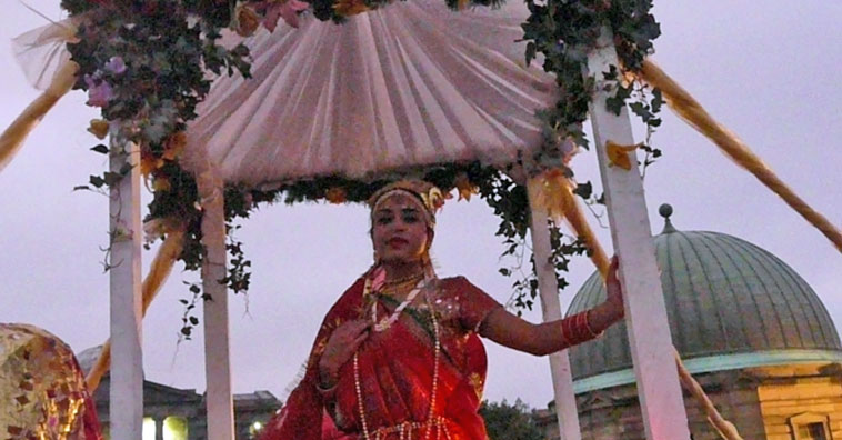 Woman in red under a white bridal bower decorated with flowers, with the Observatory behind