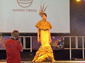 Woman in golden Harris Tweed dress starting down the catwalk with photographer in view