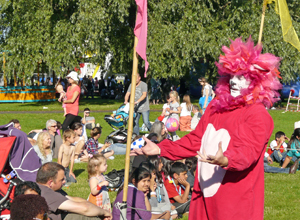 A red and pink lion performing for  seated children