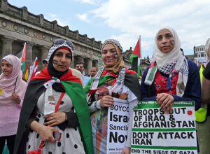 Three women in head scarves posing with placards outside the Scottish Academy