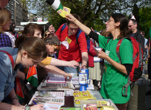 Table on Princes St, with row of people signing petitions and a  woman in a green tee shirt handing out "Boycott Israel" stickers