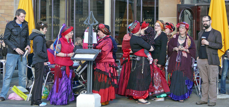 Three young women in red and black seated on a cannon raising their glasses after an evening's musical performance