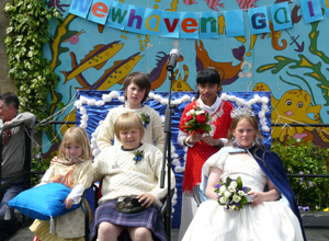 Lewis and Saba standing, with Lewis in fisherman's swearter and kilt seated with Courtney