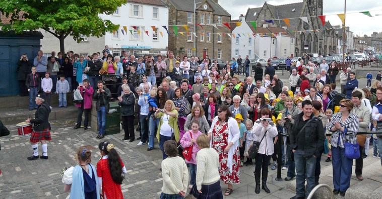 People taking photos of the Gala Queen and Fisher King with Newhaven Village in the background