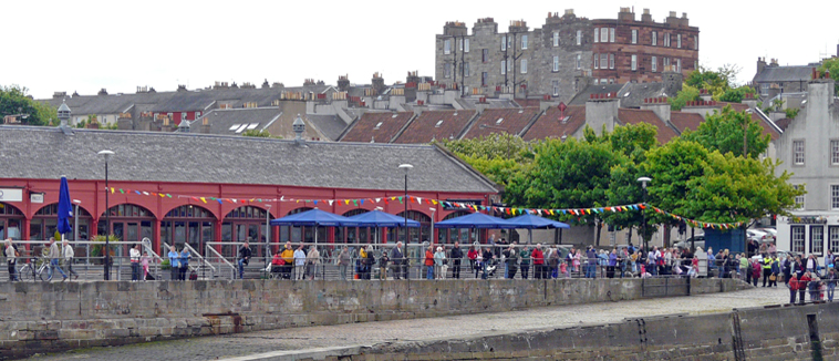 View of crowd standing in front of the Old Fishmarket looking  across Newhaven Harbour in  waiting for the Gala Queen and Fisher King
