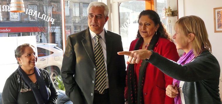 Charan Gill looking and three women talking about the plaque comemmorating the opening of the cafe