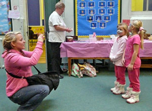 Mother in pink fleece crouching to photograph two girls in pink with cat faces