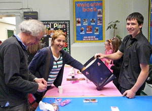 Boy from Trinity Academy holds up the blue bag with Tombola tickets in it for a woman, as her husband sifts through a handful of tickets