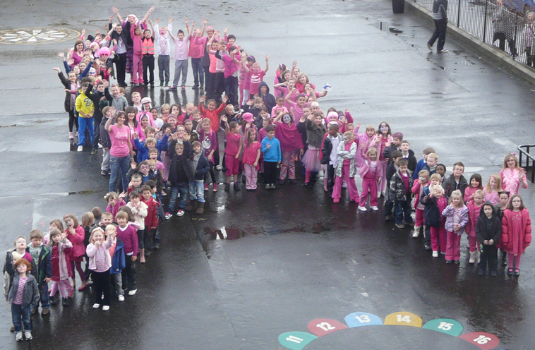 Children and staff all dressed in pink in the formation of a human ribbon waving