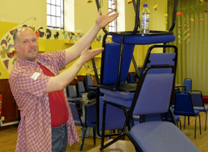 Man in red short leaved shirt with pile of blue chairs with a water bottle on the top