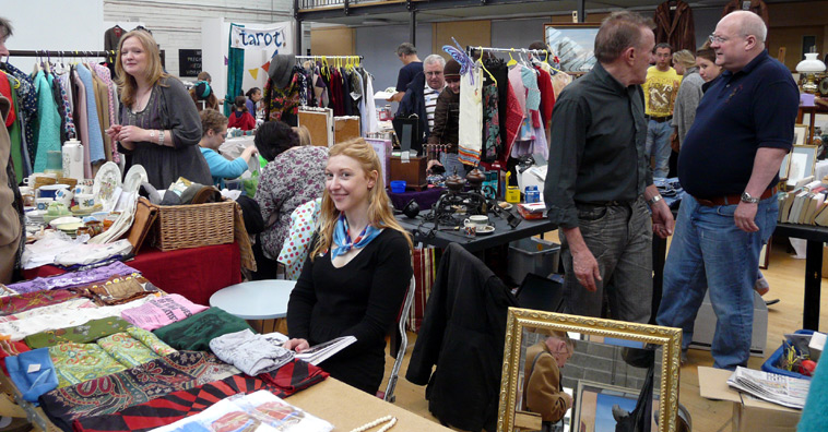 Woman sits behind a stall of scarves and shawls, with other stalls in the background