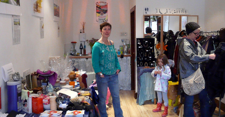 Woman in tourquoise sweater and blue jeans, standing in fitness studio as a woman looks through clothes on a rack
