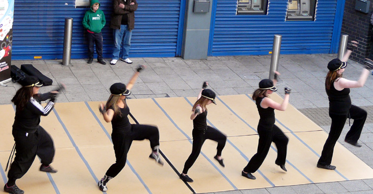 Five young women dressed in caps, black tops and dance trousers