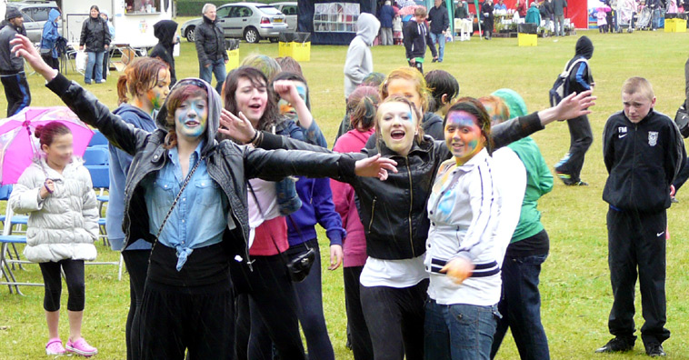 Young women with painted faces, smiling with outstretched arms as a teenage boy  watches on