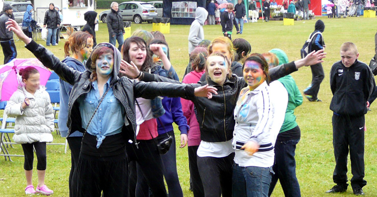 Young women with painted faces, smiling with outstretched arms as a teenage boy watches on