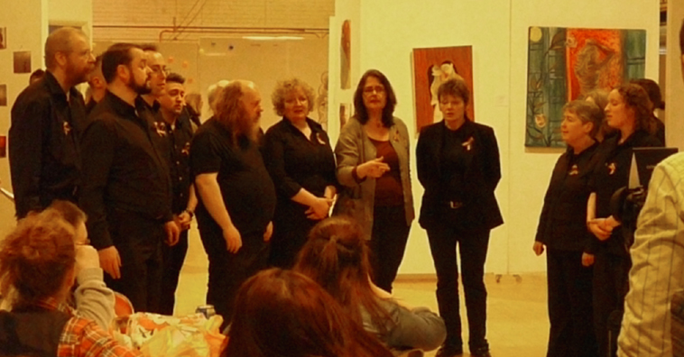 Men and women in shades of black stand singing in harmony