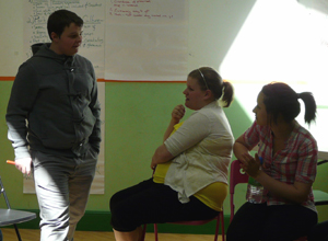 Young man in grey track suit stands talking to two seated young women