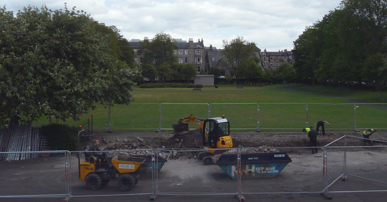 View of Montgomery St Park seen from the play park with JCBs and men clearing away rubble and digging a foundation trench