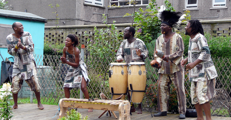 Grass Roots in African costume performing in Redbraes Garden with flats in the background