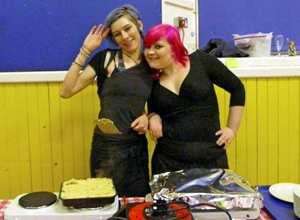 Two young women with purple and pink dyed hair posing as they serve up shepherd's pie