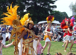 A white and gold clad woman dances with two little girls with other dancers in the background